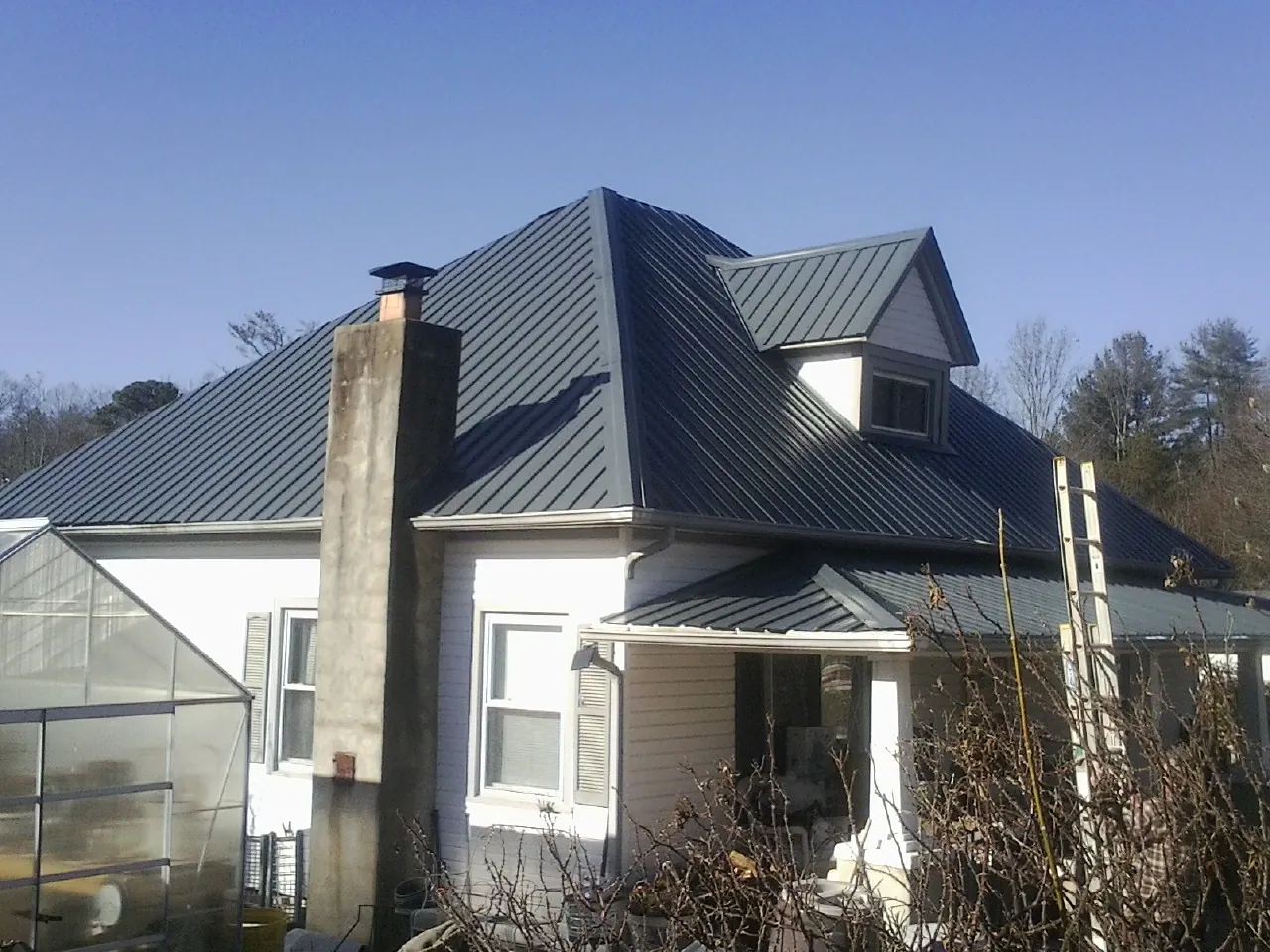 Dark blue standing seam metal roof on a white farmhouse with dormer — Slate & Tile Roof Repair by Roofing Brothers in Gordo