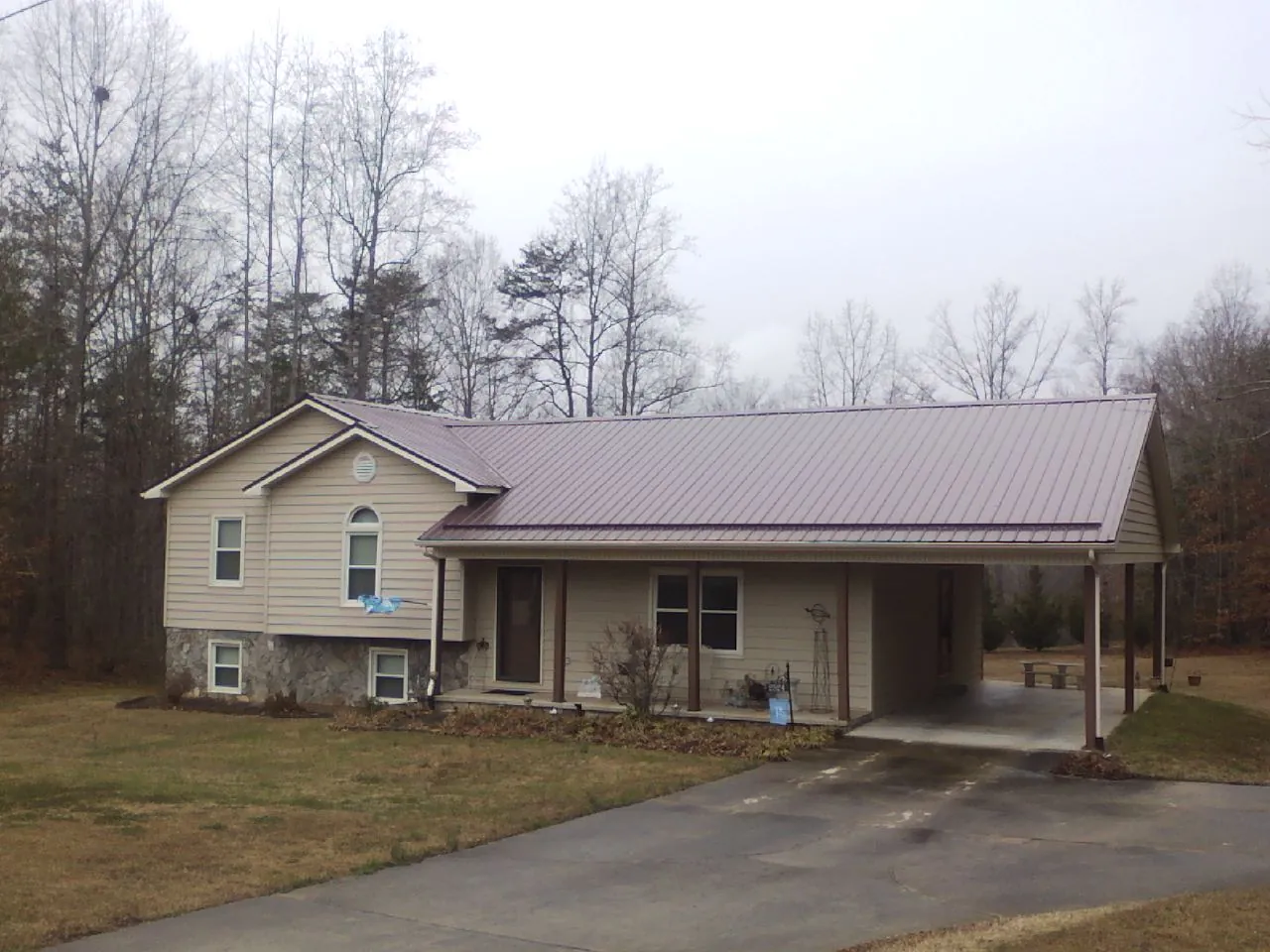 Burgundy metal roof on a tan split level home with an attached carport in Gordo