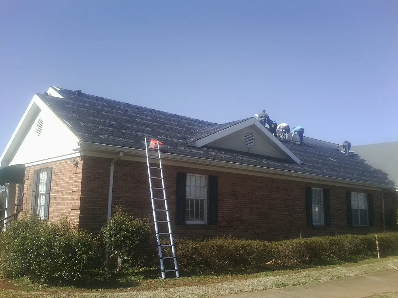 Crew tearing shingles off a brick ranch roof with a ladder set — Metal Roof Repair work by our crew in Gordo