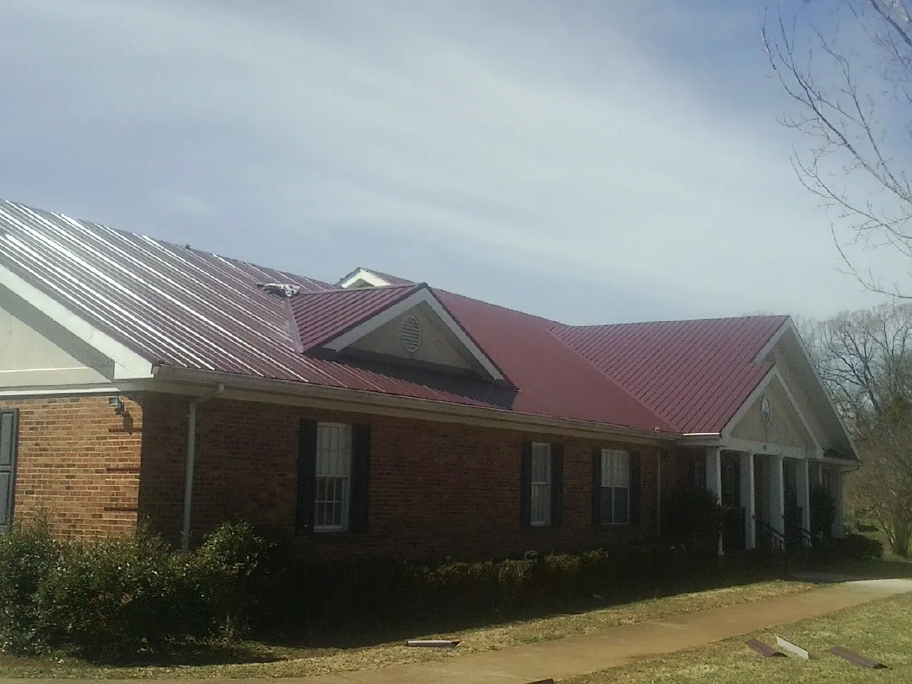 Red metal roof with gabled entries on a long brick building, from a Hail Damage Roof Repair job in Gordo