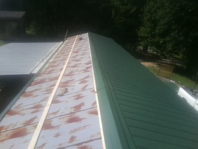 Old rusted panels beside newly installed green metal roofing — Wind Damage Roof Repair by Roofing Brothers in Gordo