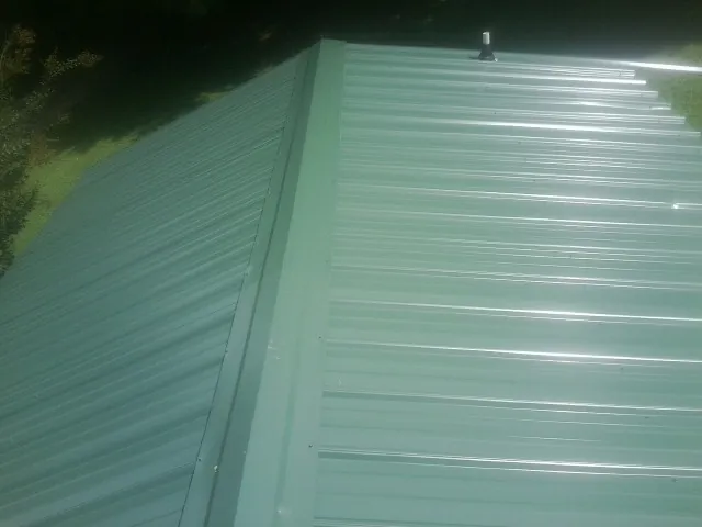 New green metal panels meeting at the ridge of a roof — Flat Roof Repair work by our crew in Gordo