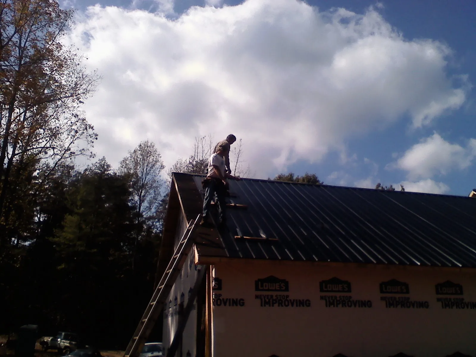 Roofer fastening dark metal panels high against a cloudy sky, from a Roof Inspection job in Gordo