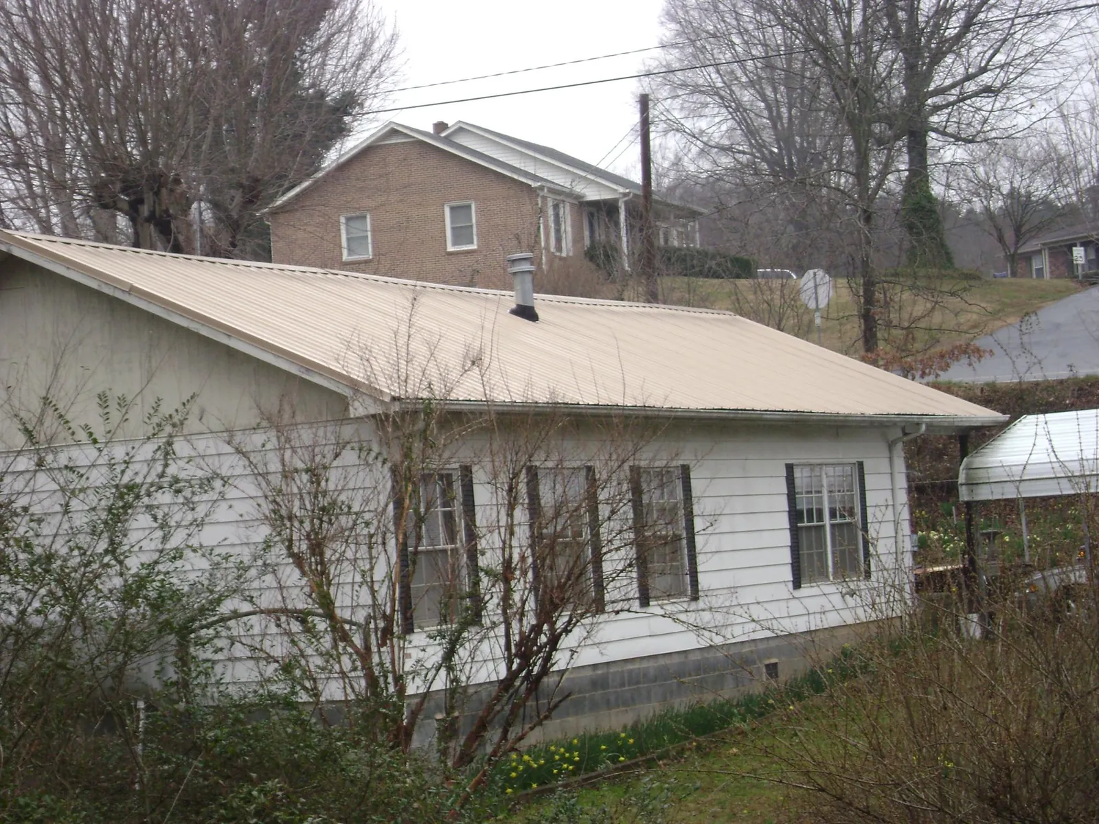 Tan metal roof on a white sided house set into a hillside — Commercial Roofing by Roofing Brothers in Gordo