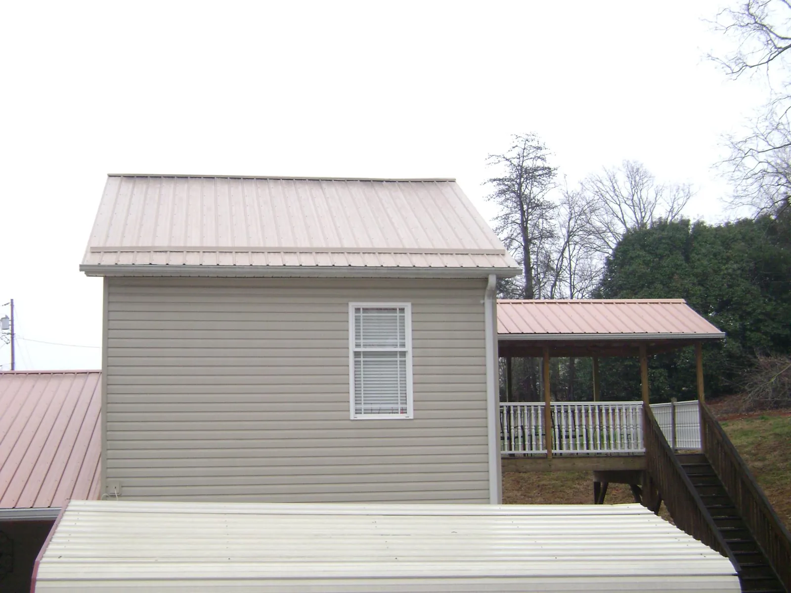 Tan metal roofs on a two story addition and attached porch, from a Roof Replacement job in Gordo